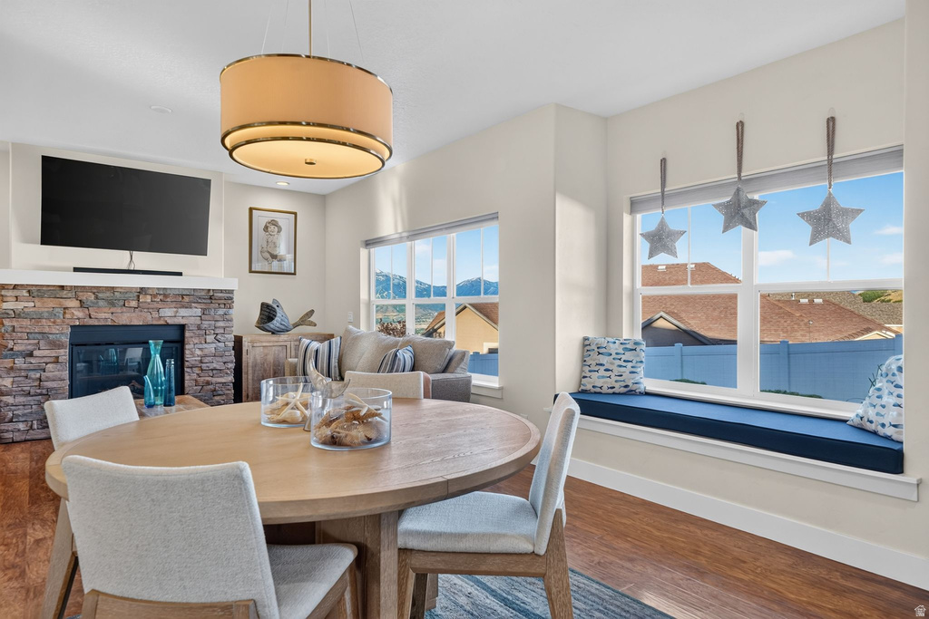 Open-concept dining and living area featuring a stone-clad fireplace, wood-finish flooring, and a built-in window seat