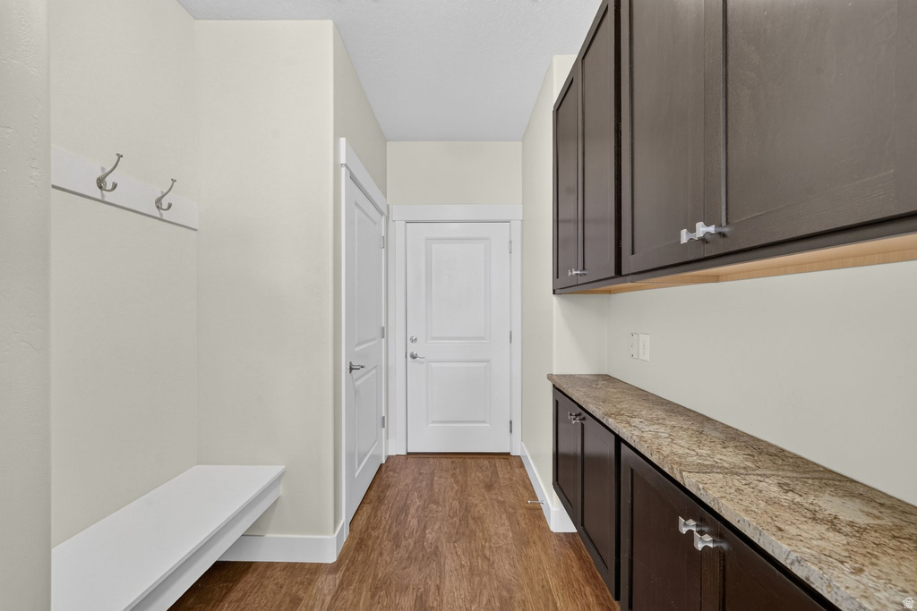 Mudroom entry featuring built-in white bench seating, wall-mounted coat hooks, wood-finish flooring, dark cabinetry with light-toned countertops, and paneled interior doors