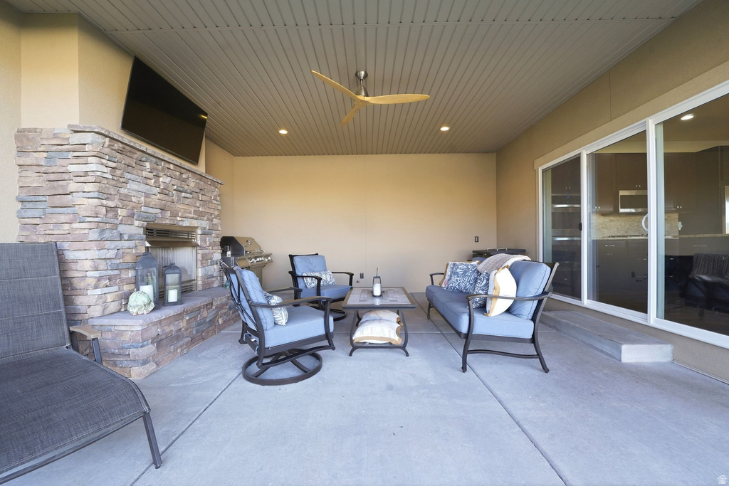 Covered outdoor patio featuring a stone-clad fireplace with an integrated media niche, a slatted ceiling with recessed lighting, and a modern ceiling fan