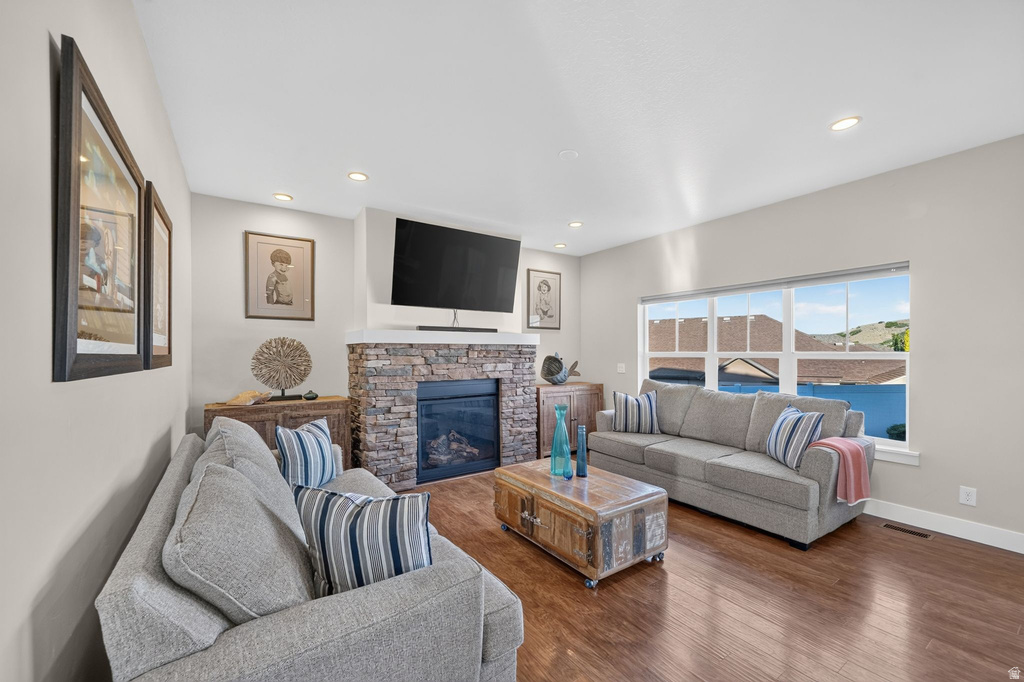 Spacious living area featuring a stone-clad fireplace with a hearth, wood-finish flooring, a large multi-pane window, recessed lighting, and light-toned walls