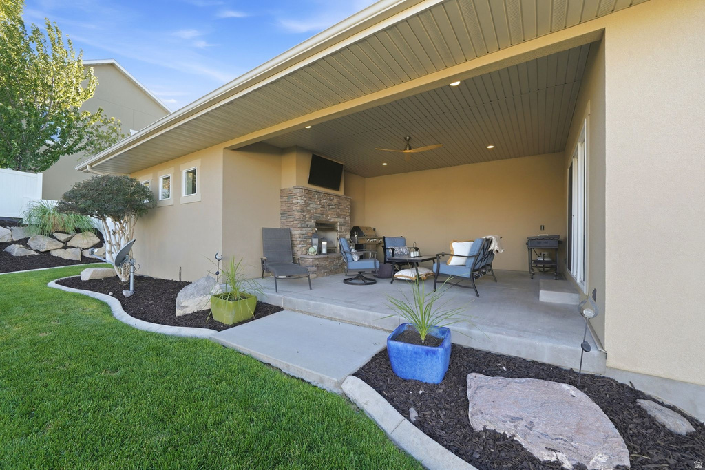Expansive covered patio featuring a stone-clad fireplace and media niche, recessed lighting, and a ceiling fan