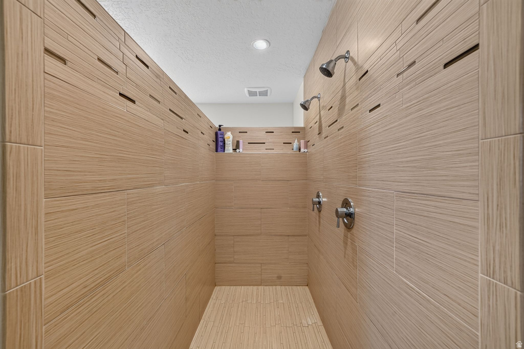 Walk-in shower featuring wood-finish tile, dual showerheads, polished chrome fixtures, and an integrated shelf