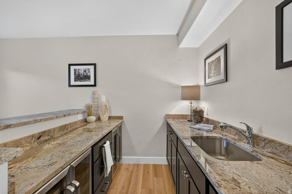 Wet bar featuring granite countertops, a stainless steel undermount sink, dark wood cabinetry, integrated beverage refrigeration, and wood-finish flooring