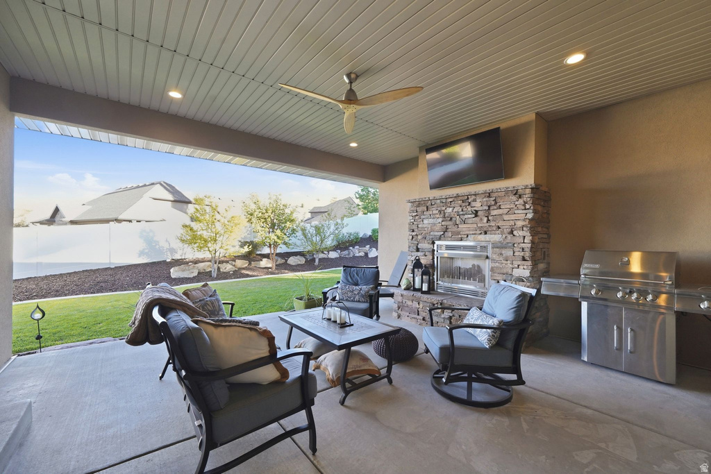 Covered patio featuring a stone-clad fireplace, built-in stainless steel grill, ceiling fan, and recessed lighting