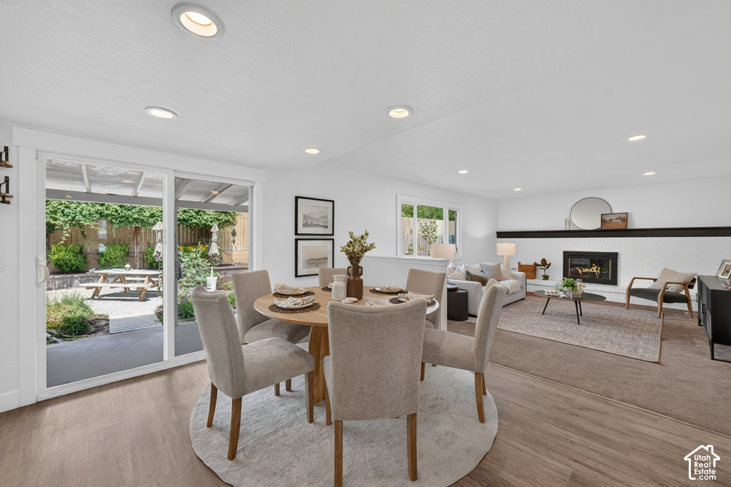 Open-concept living area with wood-finish flooring, recessed lighting, and a white brick fireplace with a black mantel