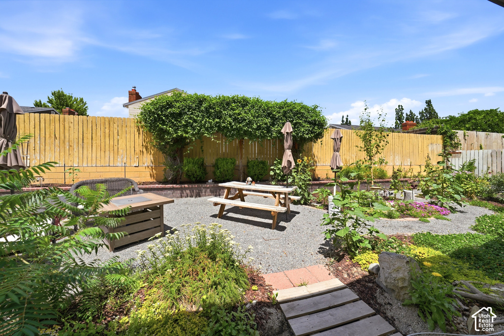 Expansive backyard featuring a gravel patio area with a picnic table, a built-in fire pit, a perimeter fence with mature foliage, and diverse plant beds throughout