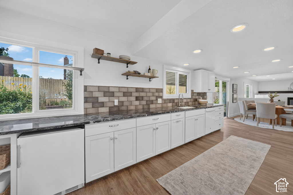 Spacious kitchen featuring extensive white cabinetry, dark stone countertops, subway tile backsplash, recessed lighting, and wood-finish flooring