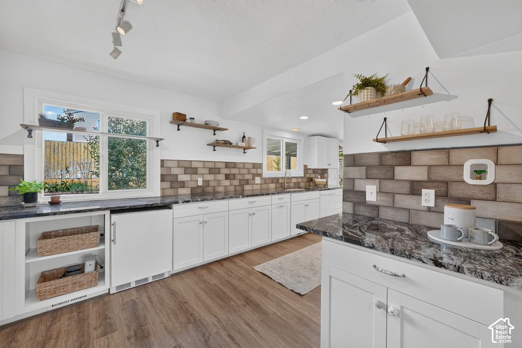 Spacious kitchen featuring extensive white cabinetry, dark stone countertops, a multi-tone tile backsplash, wood-finish flooring, and open shelving