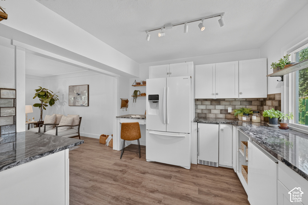 Kitchen featuring wood-finish flooring, white cabinetry, dark stone countertops, and a subway tile backsplash