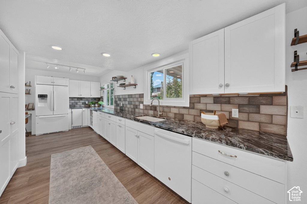 Modern kitchen featuring white cabinetry, dark granite-finish countertops, wood-finish flooring, and a subway tile backsplash