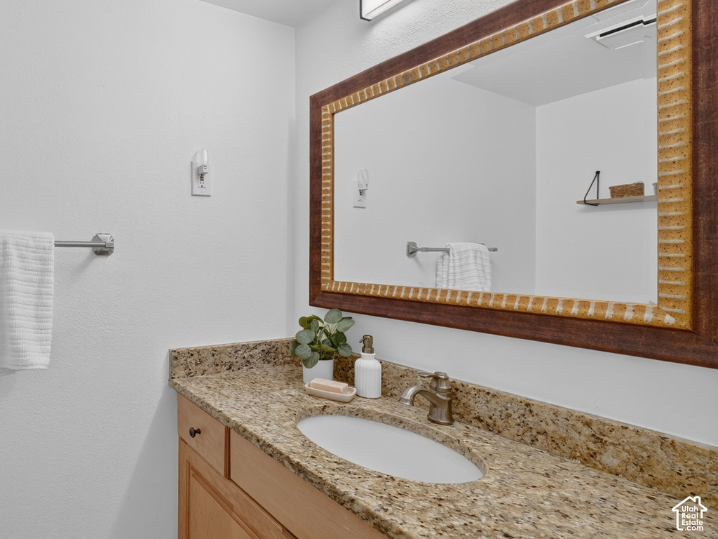 Wood-finish vanity with panel-front cabinetry and dark bronze hardware, featuring a granite countertop with an integrated oval sink and an antique brass-finish faucet