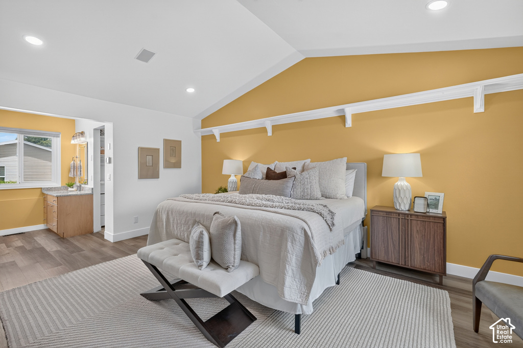 Vaulted ceiling bedroom with recessed lighting, wood-finish flooring, and a vanity area featuring a rectangular sink, stone countertop, and wood-finish cabinetry