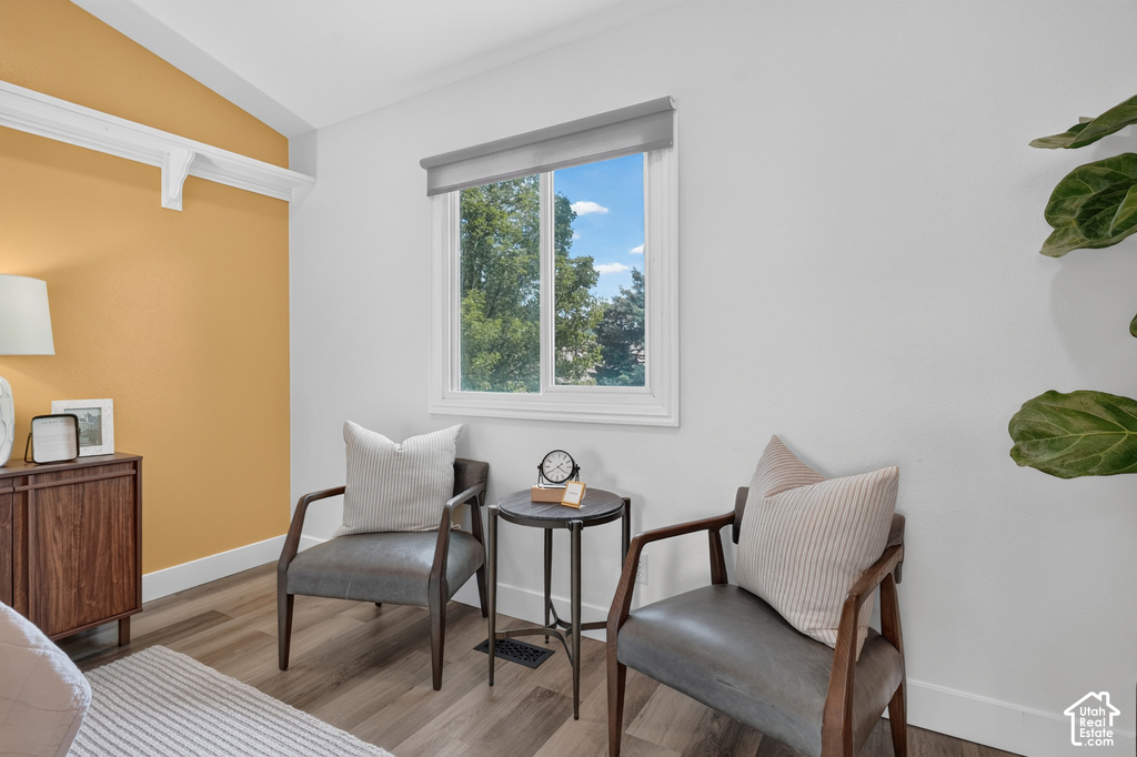 Interior space featuring a window with exterior views, wood-finish flooring, a vaulted ceiling with white trim, and a warm accent wall