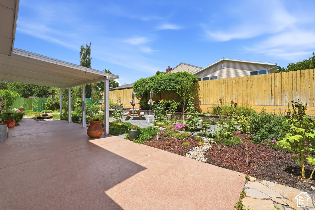 Expansive rear patio featuring a covered area with support pillars, concrete flooring, and an adjacent landscaped garden bed