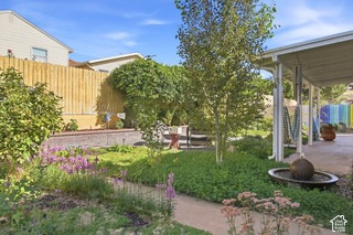 Landscaped backyard featuring a covered patio, garden beds with various plantings, a decorative water feature, and a privacy fence