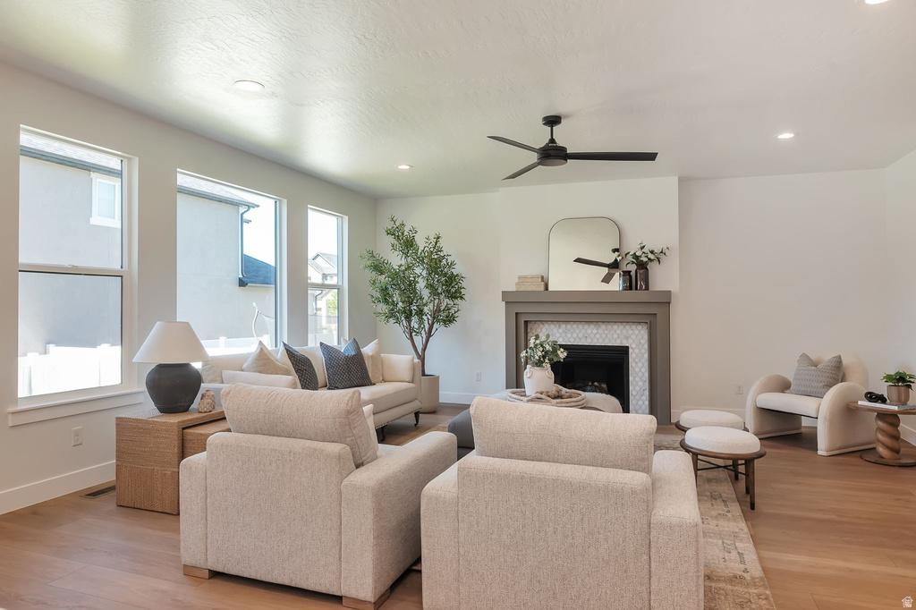 Spacious living area featuring wood-finish flooring, a contemporary fireplace with decorative tile surround and mantel, a modern ceiling fan, recessed lighting, and multiple large windows