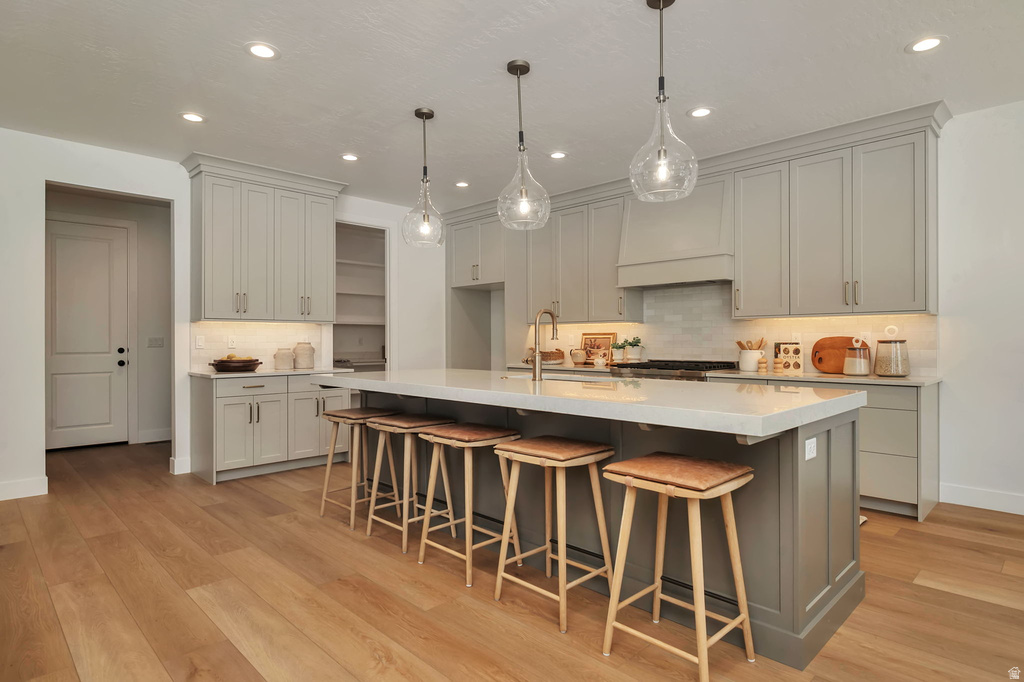 Open-concept kitchen featuring an expansive center island with seating, pendant lighting, shaker-style cabinetry, wood-finish flooring, and recessed lighting