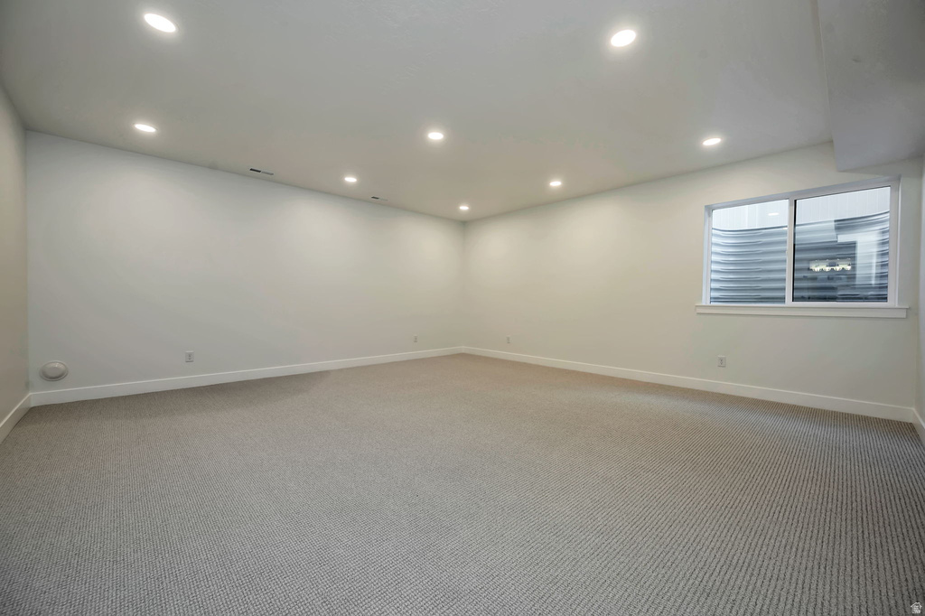 Spacious room with recessed lighting, light gray textured carpeting, white walls, white baseboards, and a window with a window well