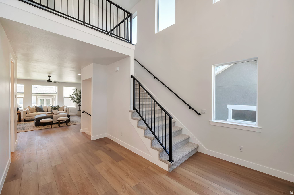 Foyer featuring wood-finish flooring, a carpeted staircase with black metal railings, and a two-story ceiling with high windows