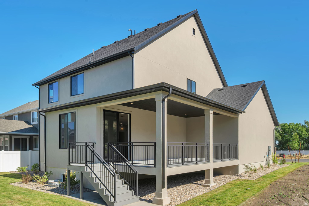 Rear exterior featuring a covered patio, dark gray composite decking, black metal railing, and light stucco siding
