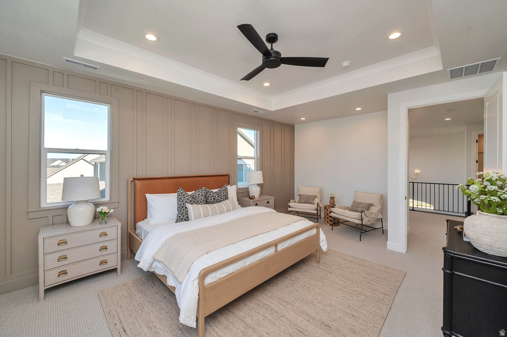 Bedroom featuring a tray ceiling with recessed lighting and a ceiling fan, wall paneling, two double-hung windows, and light-toned carpeting