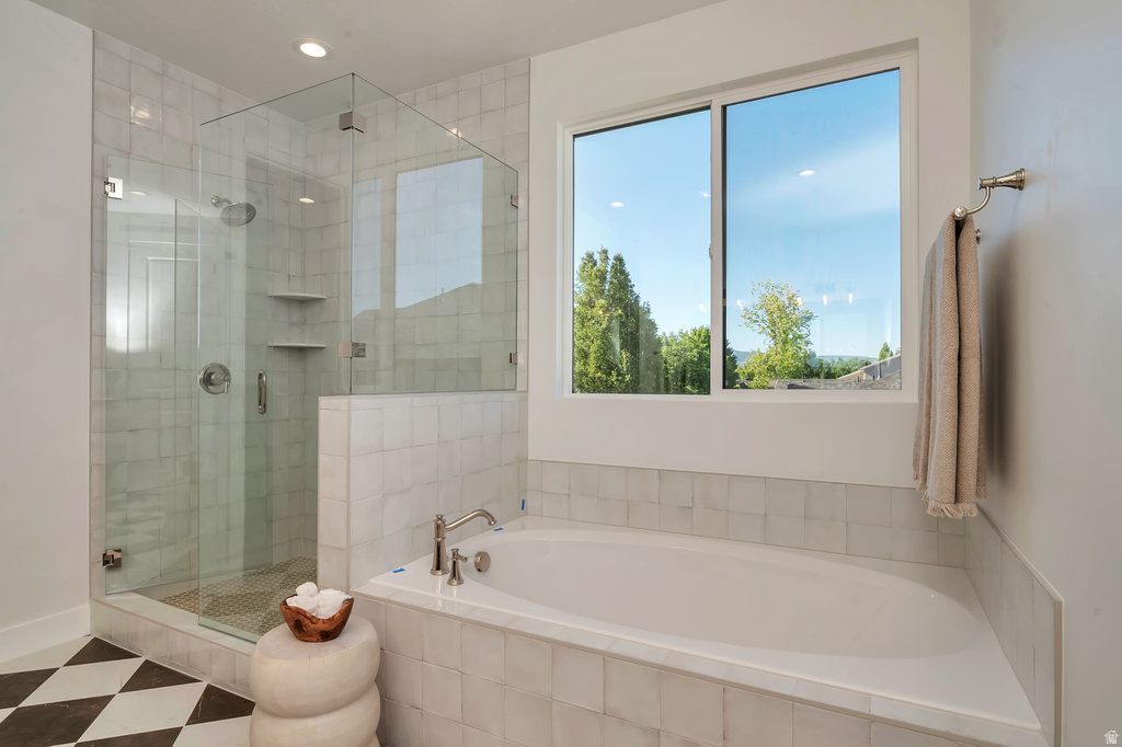 Spacious bathroom featuring a built-in soaking tub, a large glass-enclosed shower with tile surround, a checkered floor, and a generous window