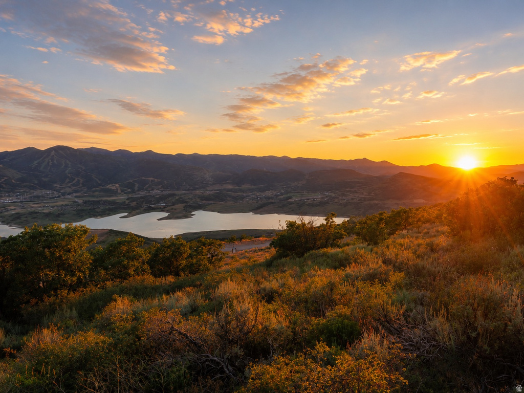 Expansive mountain landscape featuring a lake, natural foliage, and a dramatic sunset
