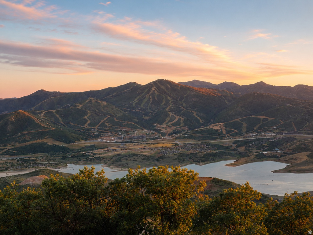 Expansive mountainous landscape featuring a large body of water, distant structures, and visible ski trails