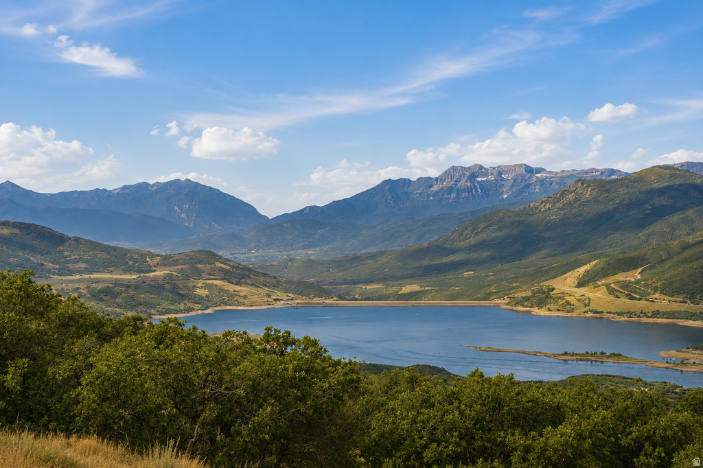 Expansive mountain landscape featuring a large body of water, lush green foliage, and distant snow-capped peaks under a clear blue sky