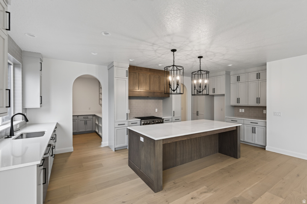 Expansive kitchen featuring a large central island with a white countertop, two black caged chandeliers, light wood-finish flooring, and a mix of light gray and wood-finish cabinetry