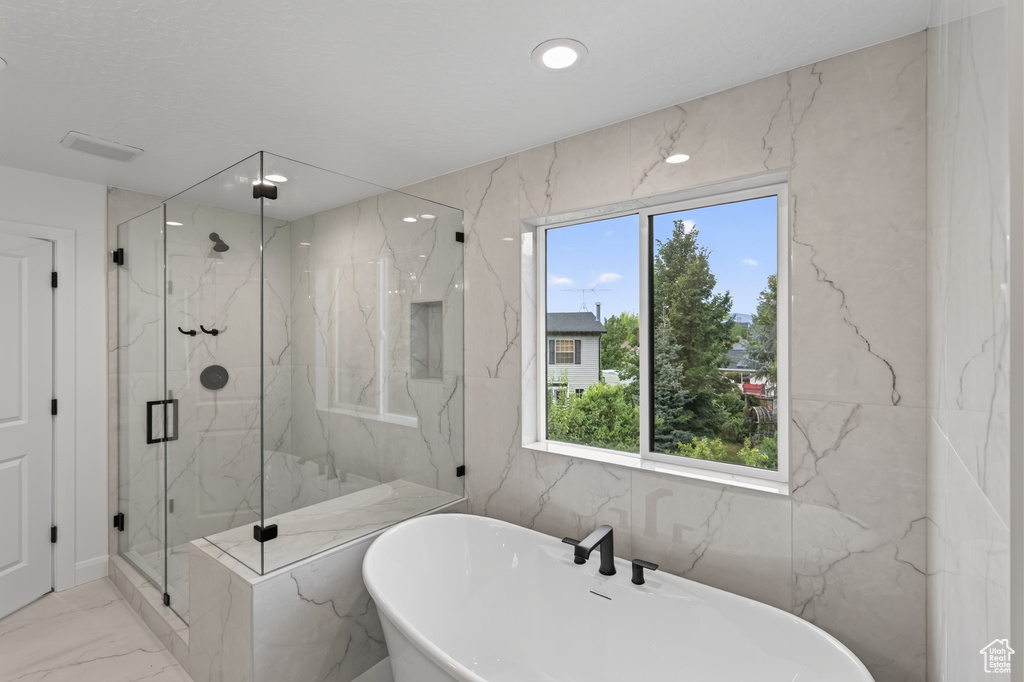 Bathroom featuring a freestanding soaking tub with matte black fixtures, a spacious glass-enclosed shower with an integrated bench and matte black hardware, and large format tiled walls