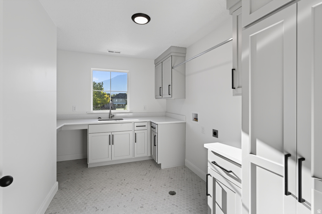 Bright laundry room featuring white cabinetry with black hardware, an undermount sink, and light-colored countertops