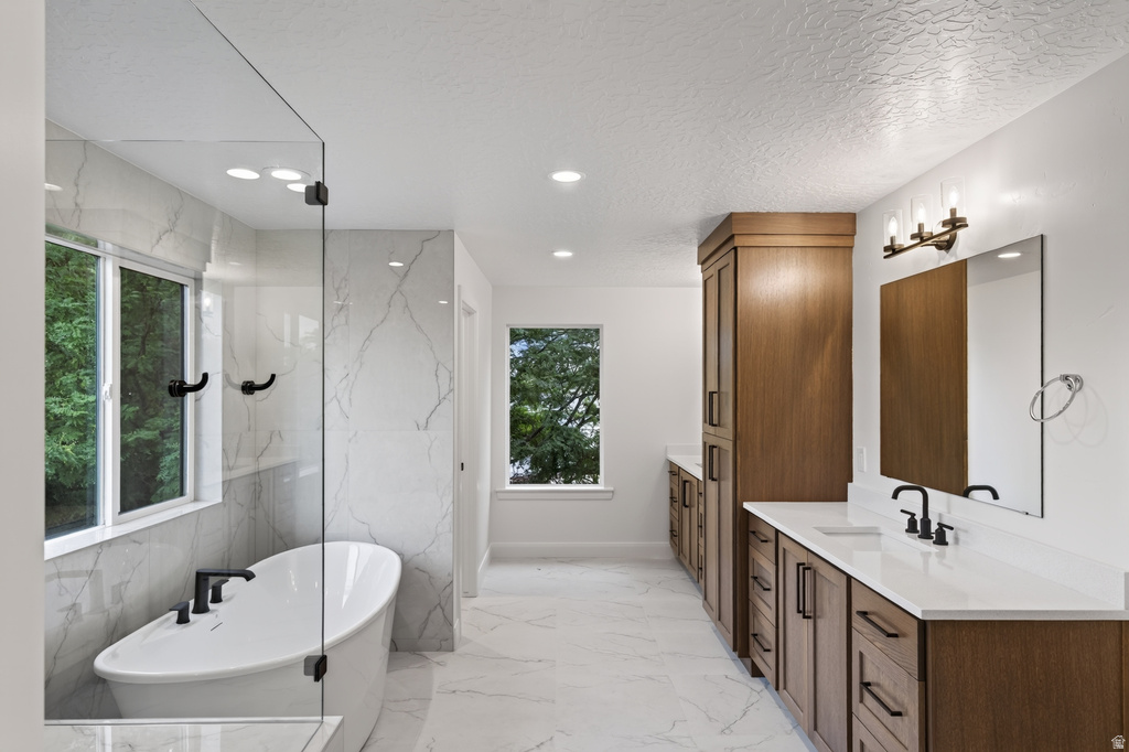 Spacious bathroom featuring a freestanding soaking tub, glass-enclosed shower, dual vanity with quartz countertops, custom wood cabinetry, and large format marble-look tile flooring