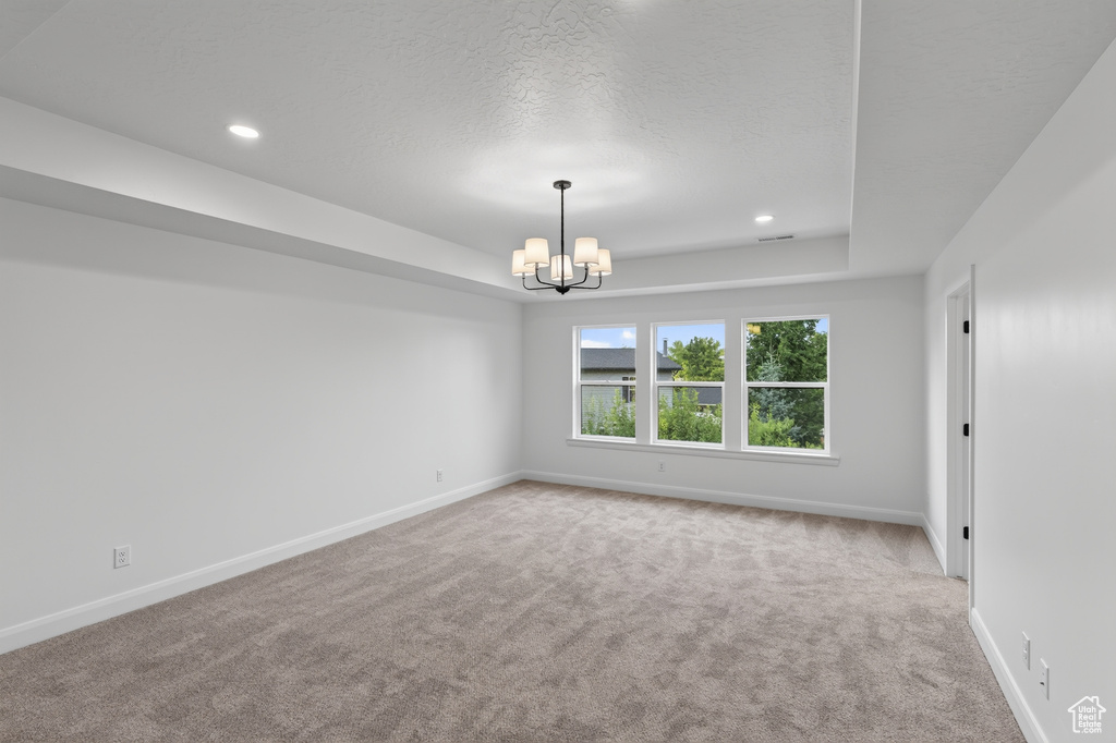 Spacious room featuring neutral carpeting, white walls, and a tray ceiling with recessed lighting