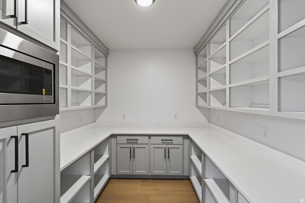 Walk-in pantry featuring extensive open shelving, perimeter countertops, built-in lower cabinetry, a built-in microwave, and wood-finish flooring