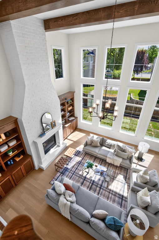 Two-story living area featuring a white brick fireplace with a mantel, exposed wood ceiling beams, a multi-pane window wall, and wood-finish flooring