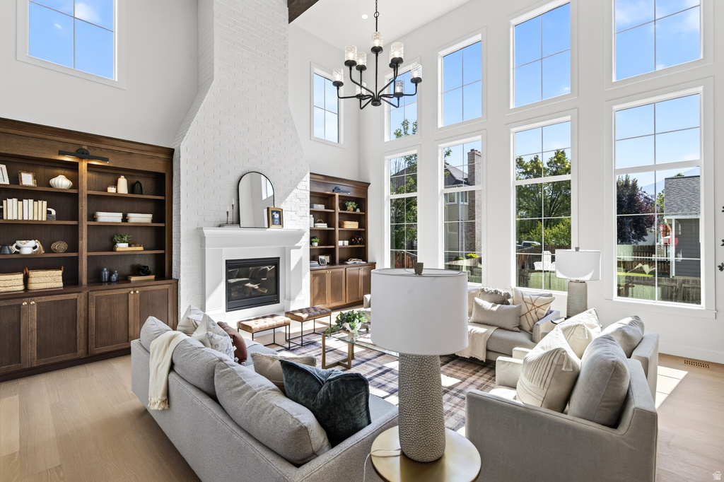 Two-story living area featuring a white brick fireplace with a mantel, built-in dark wood shelving units, light wood-finish flooring, and multiple tall windows