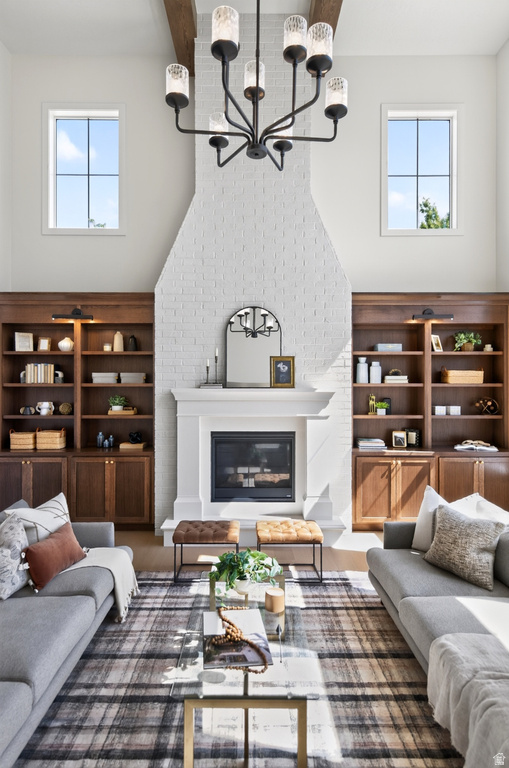 Vaulted living space featuring a white brick fireplace with a classic mantel, built-in wood-finish shelving, and a prominent dark metal chandelier