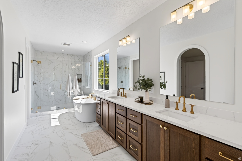 Bathroom featuring a freestanding soaking tub, a large glass-enclosed shower with marble-look tile, a double vanity with dark wood cabinetry, white countertops, and gold-finish fixtures
