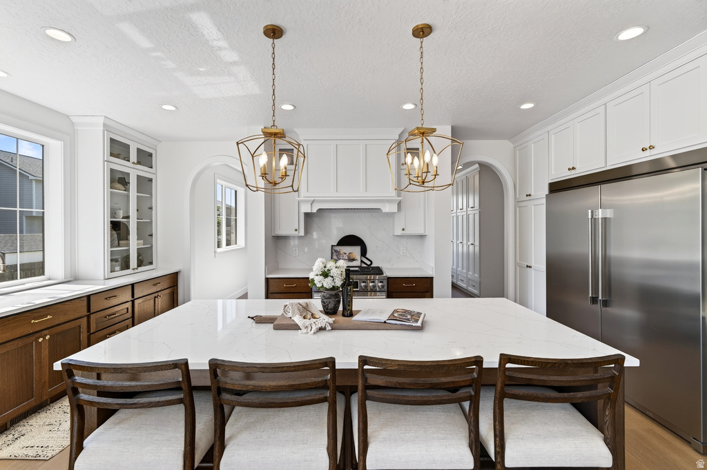 Spacious kitchen featuring a large central island with seating, pendant lighting, stainless steel appliances, white upper cabinetry, and wood-finish lower cabinetry