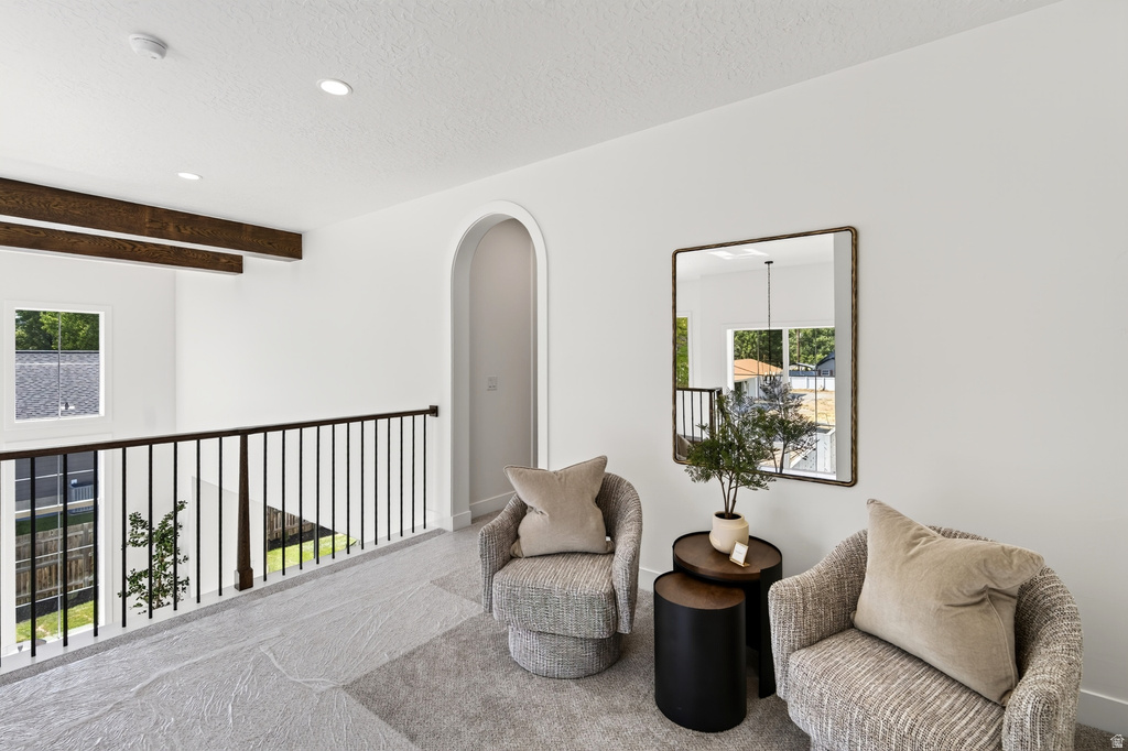 Upper-level landing featuring a sleek black metal railing, exposed wood-finish beams, a soft gray carpet, recessed lighting, and a graceful arched entryway