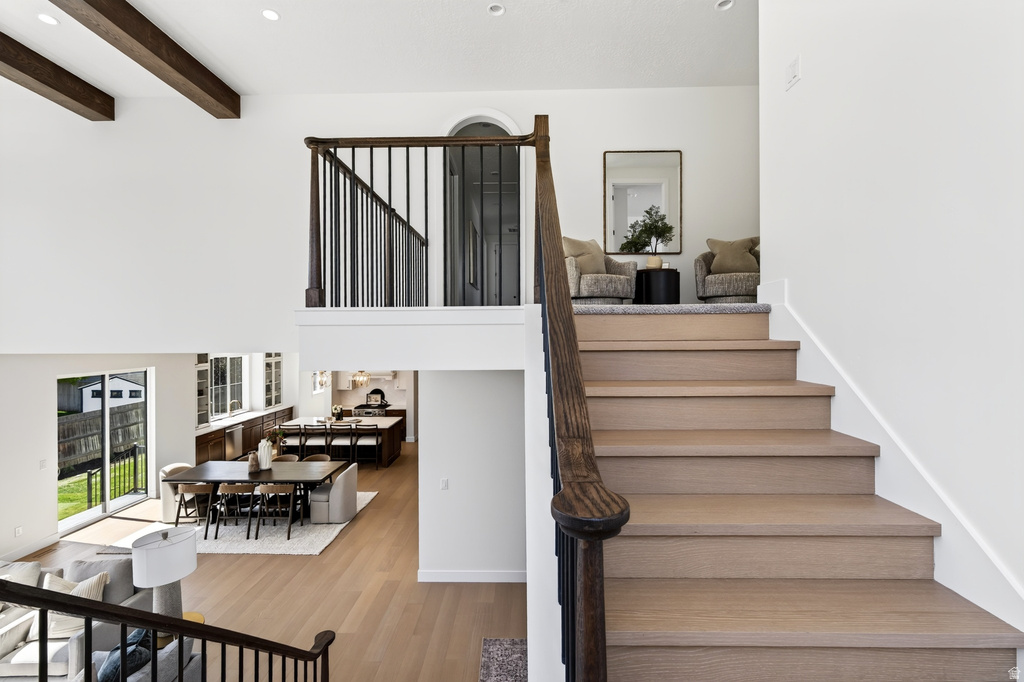 Multi-level interior featuring wood-finish flooring, white walls, dark wood-tone exposed beams, an open-concept dining area, and a kitchen with dark wood-tone cabinetry