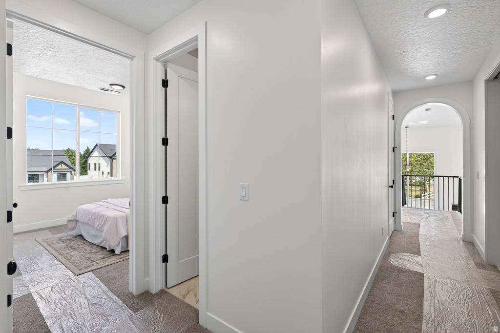 Hallway featuring recessed lighting, an arched entryway, and dark metal railing