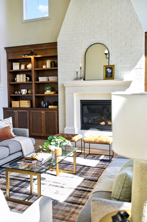 Living area featuring a floor-to-ceiling brick fireplace with a hearth, dark wood built-in shelving, a large window, wood-finish flooring, and a patterned area rug