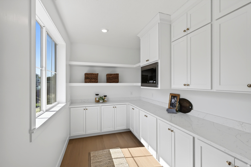 Bright utility room featuring white shaker-style cabinetry, light-toned countertops, open shelving, and wood-finish flooring