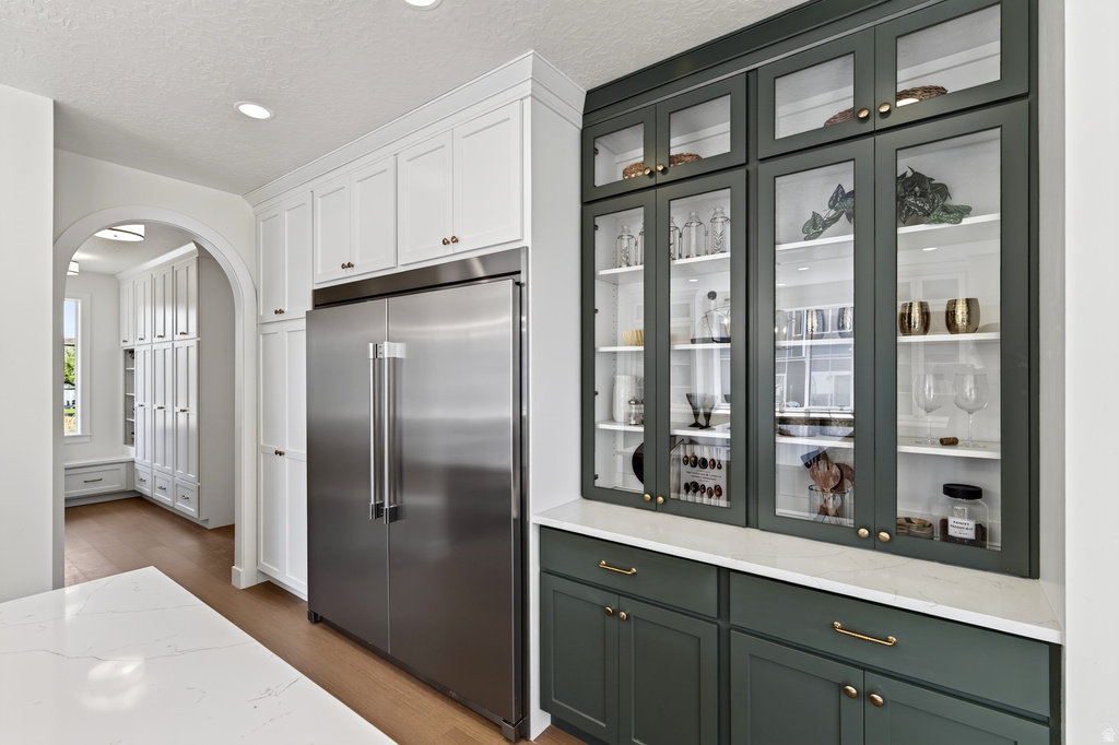 Stainless steel refrigerator with custom built-in cabinetry, including white upper cabinets and deep green glass-front display cabinets