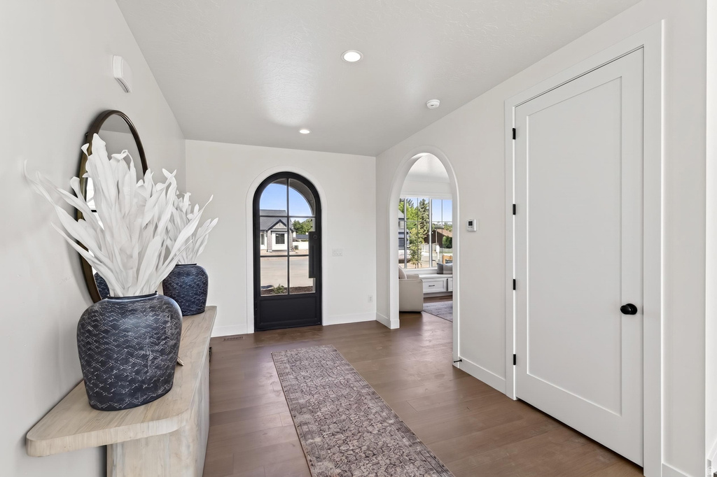 Entryway featuring a black arched glass-paneled door, wood-finish flooring, recessed lighting, and an arched doorway leading to another room