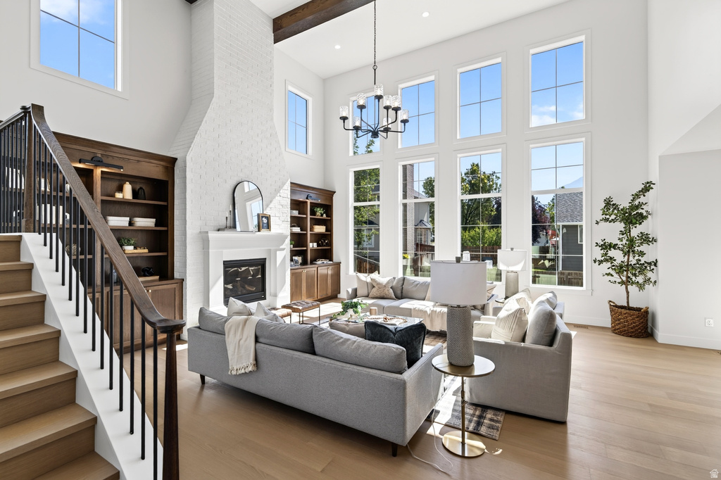 Two-story living area featuring a fireplace with white brick surround, built-in shelving, wood-finish flooring, and a chandelier