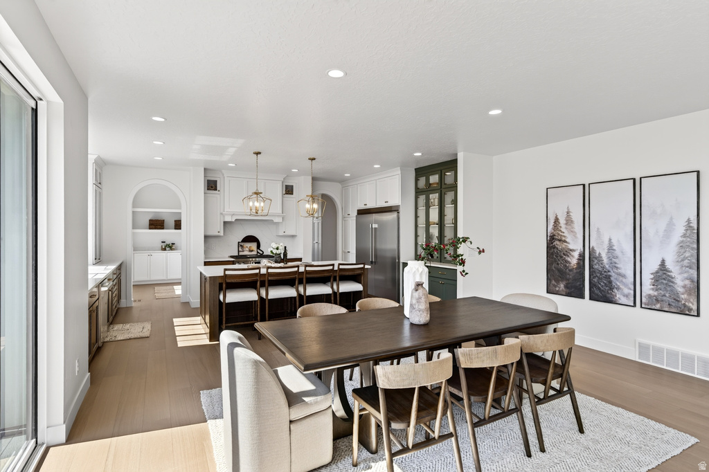 Open-concept kitchen and dining area featuring light wood-finish flooring, recessed lighting, a built-in kitchen island with seating, a sliding glass door, and a dedicated beverage station with built-in appliances