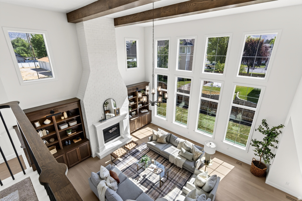 Two-story living area featuring a white brick fireplace with a mantel, built-in shelving, dark wood ceiling beams, and a wall of tall windows